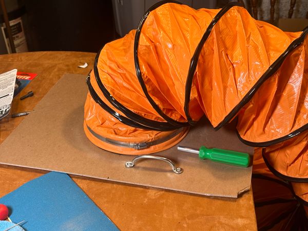 An orange ducting hose, clamped to hardware for a paint booth venting solution.